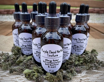 May include: Multiple 2-ounce bottles of Purple Dead Nettle Tincture, a natural remedy for allergy relief, anti-inflammatory, and anti-bacterial benefits. The bottles are arranged on a white lace tablecloth with green leaves.