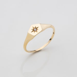 May include: A gold signet ring with a star-shaped design and a small clear stone in the center.