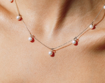 Puede incluir: Un delicado collar de cadena dorada con cinco colgantes de perlas blancas.