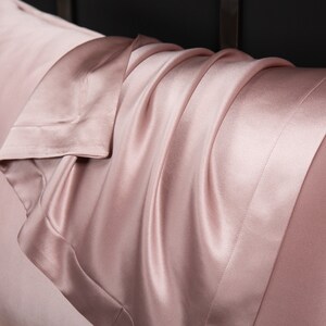 May include: A close-up of a soft, pink satin pillowcase. The fabric is smooth and luxurious, with a subtle sheen.