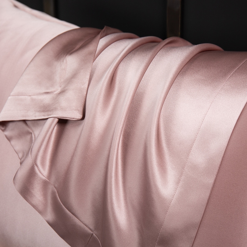 May include: A close-up of a soft, pink satin pillowcase. The fabric is smooth and luxurious, with a subtle sheen.