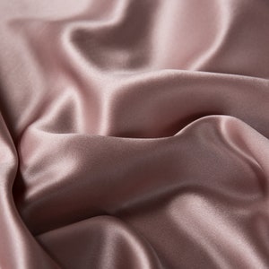 May include: Close-up of a soft, smooth, and silky fabric in a dusty rose color. The fabric is draped and folded, creating a luxurious and elegant look.
