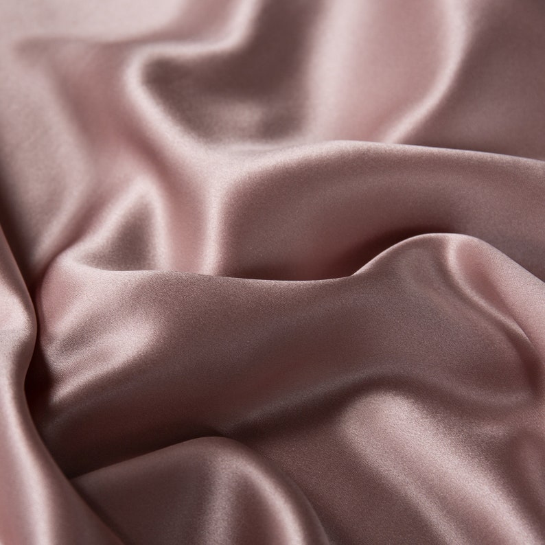 May include: Close-up of a soft, smooth, and silky fabric in a dusty rose color. The fabric is draped and folded, creating a luxurious and elegant look.