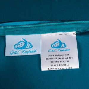 May include: White care label with blue text and a logo that says "DOL Comfortable" and instructions for washing 100% mulberry silk. The label is on a teal fabric background.