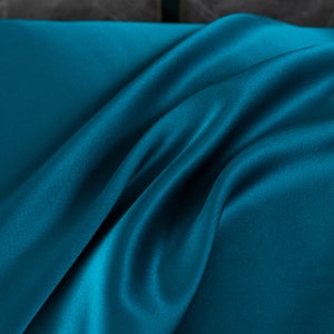 May include: A close-up of a teal blue satin fabric with soft, flowing folds.