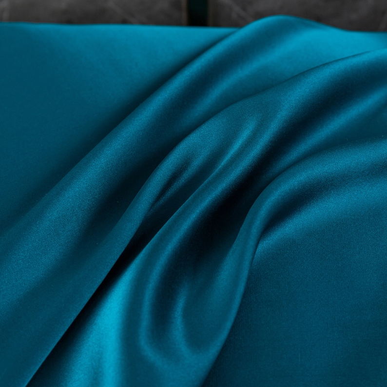 May include: A close-up of a teal blue satin fabric with soft, flowing folds.