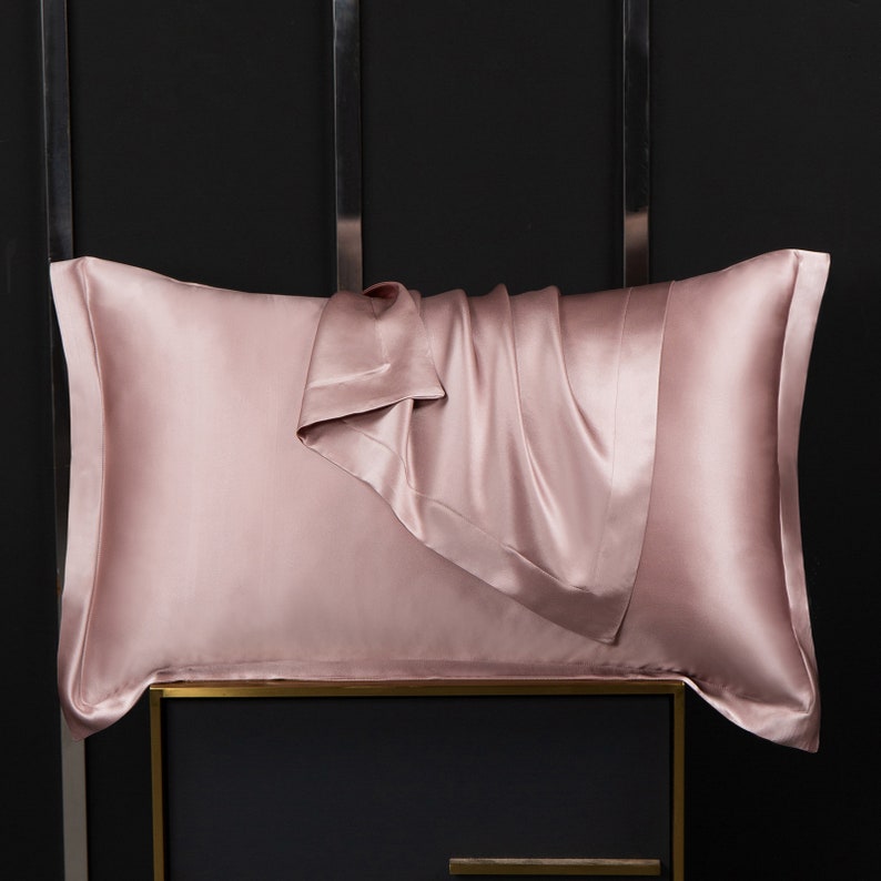 May include: A blush pink silk pillowcase with a folded edge. The pillowcase is made of soft, luxurious silk and is designed to help prevent wrinkles and hair breakage.