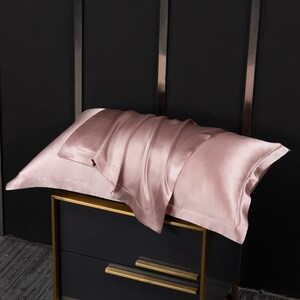 May include: A soft, pink silk pillowcase folded on a black nightstand with gold trim.