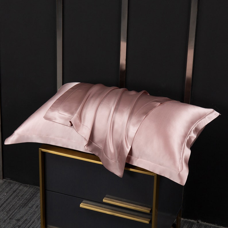 May include: A soft, pink silk pillowcase folded on a black nightstand with gold trim.
