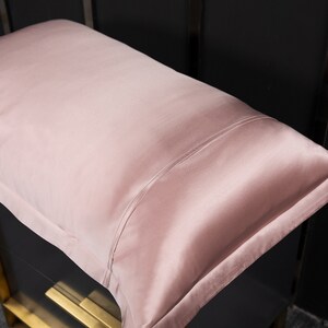 May include: A soft, blush pink silk pillowcase. The pillowcase is smooth and has a subtle sheen.