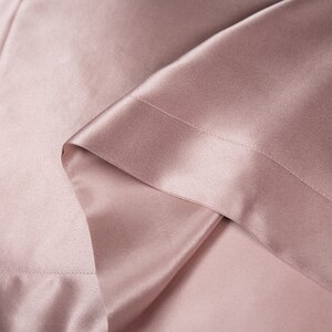 May include: A close-up of a soft, smooth, blush-colored satin fabric. The fabric is folded and has a subtle sheen.