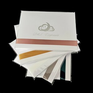 May include: A stack of white cards with a pink ribbon, a gold ribbon, a white ribbon, a gray ribbon, and a dark blue ribbon. The top card has a silver cloud with stars and a crescent moon and the text "D&L Comfortable".