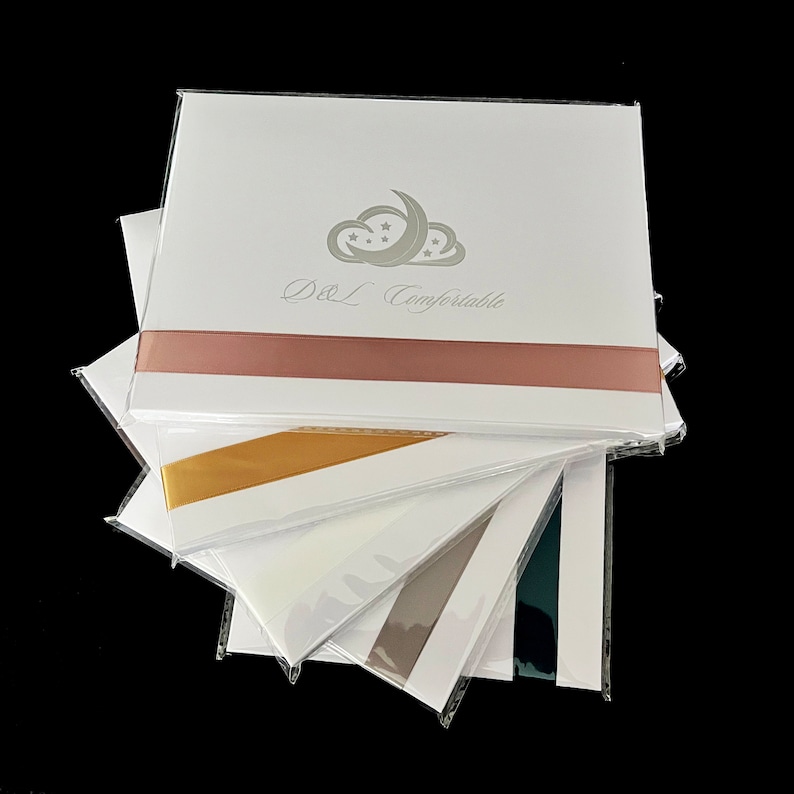 May include: A stack of white cards with a pink ribbon, a gold ribbon, a white ribbon, a gray ribbon, and a dark blue ribbon. The top card has a silver cloud with stars and a crescent moon and the text "D&L Comfortable".
