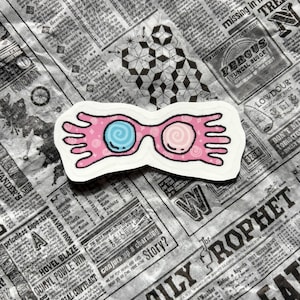 May include: A sticker depicting pink-framed glasses with blue and pink spiral lenses. The glasses have a whimsical design with elongated arms. The sticker is set against a backdrop of newspaper print.