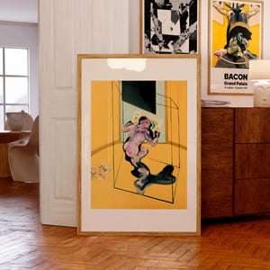 May include: A framed print of a painting by Francis Bacon. The painting depicts a nude figure in a yellow room with a glass box. The title of the painting is "Bacon Grand Palais" and the dates "27 octobre - 19 janvier 1972" are printed below the title.
