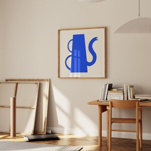 Puede incluir: Una impresión artística enmarcada con un diseño abstracto azul de una tetera sobre un fondo crema. La obra de arte se presenta en un marco de madera clara, que complementa el estilo moderno. La impresión está colgada en una pared de color neutro.