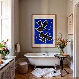 May include: A framed wall art print featuring two black stylized birds against a vibrant blue background with a small white crescent moon and stars, displayed above a white clawfoot bathtub in a room with light gray walls and herringbone floors.