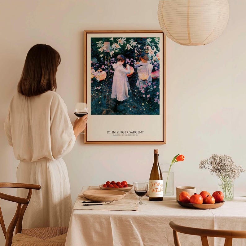 May include: A framed art print of John Singer Sargent's Carnation, Lily, Lily, Rose painting, featuring two figures in white dresses in a garden. The print is displayed on a wall above a dining table set with a wine bottle, glasses, and fruit.