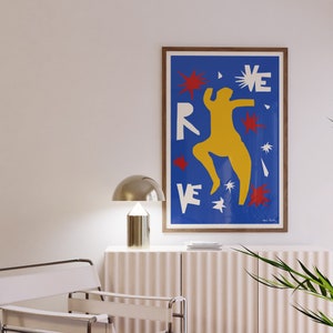 May include: A framed poster with a blue background and a yellow figure dancing. The poster has the word "REVE" in white letters and red and white stars.