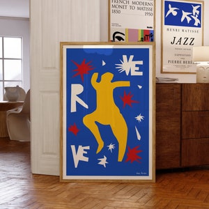 May include: A blue and yellow abstract art print with a red, white, and yellow figure dancing. The background is blue with white and red stars. The print is framed in a wooden frame.