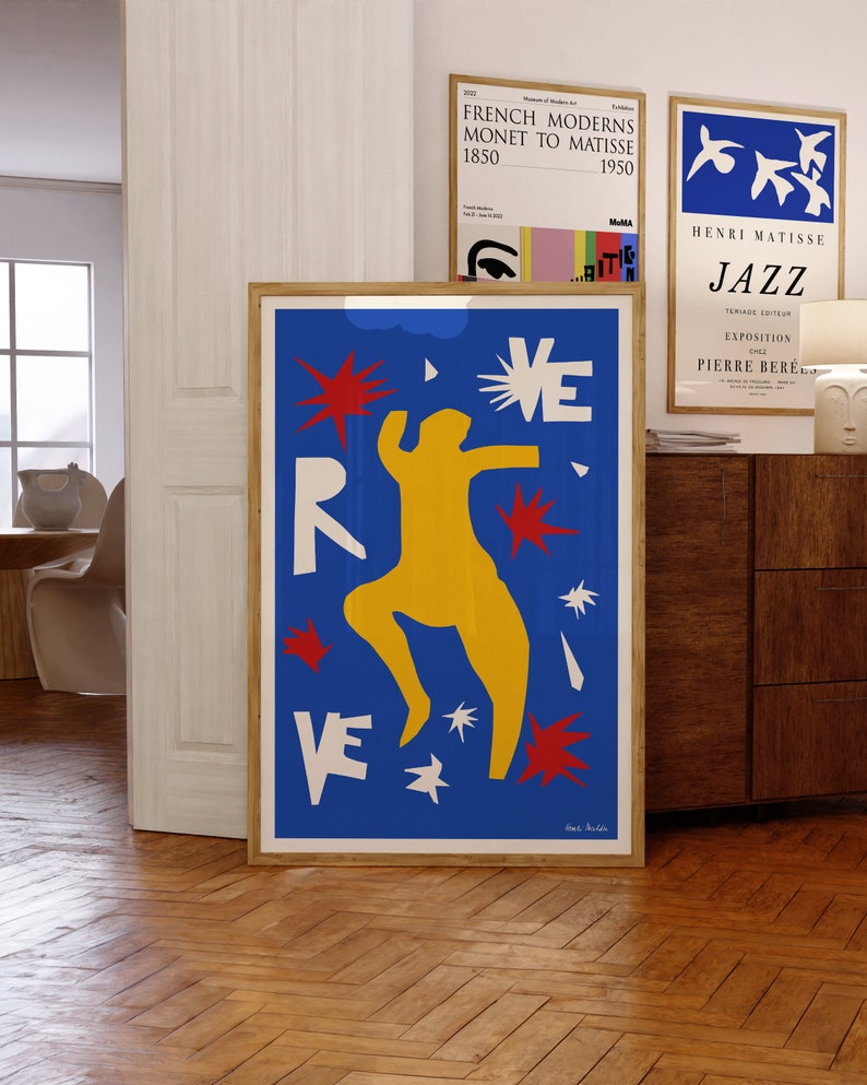 May include: A blue and yellow abstract art print with a red, white, and yellow figure dancing. The background is blue with white and red stars. The print is framed in a wooden frame.