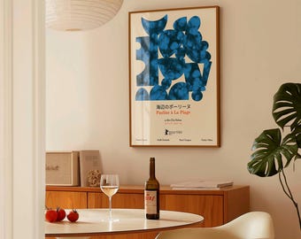 May include: A framed poster with a blue abstract design hangs on a wall. A bottle of wine, a wine glass, and three tomatoes sit on a white table. A wooden cabinet and a plant are also visible.