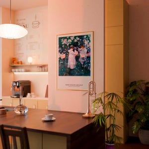 May include: A framed art print featuring John Singer Sargent's painting of two figures in a garden, displayed on a wall. The print shows a white border with the artist's name in black text at the bottom, enclosed in a thin gold-colored frame.