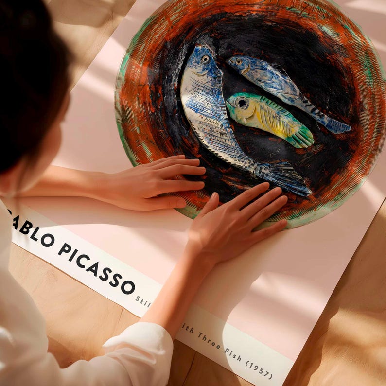 May include: A poster featuring a still life artwork of three fish in a bowl, with the text "Pablo Picasso" and "Still Life with Three Fish (1957)". The fish are blue, yellow, and green, set against a dark background.