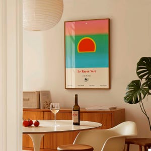 May include: A framed art print with a colorful abstract design, featuring a red sun shape against a blue and green background. The print is labeled "Le Rayon Vert" in white text. A bottle of wine and a glass are on a table.