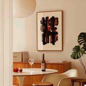 Puede incluir: Lámina de arte abstracto enmarcada en madera. La obra presenta pinceladas negras y naranjas sobre un fondo crema. Una botella de vino, una copa de vino y tomates están sobre una mesa blanca. Una habitación de estilo moderno de mediados de siglo.