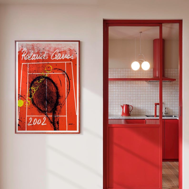 May include: Framed art print featuring a tennis court design with the text "Roland Garros 2002" in white. The artwork has a red background with white lines and black and yellow accents. The print is displayed on a white wall.