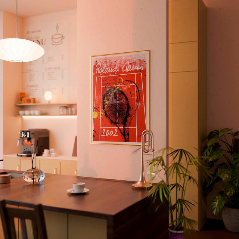 May include: A framed art print featuring a tennis racket and court design with the text "Roland Garros 2002" on a red background. The image is in a gold frame, and the scene includes a trumpet and a coffee shop setting.
