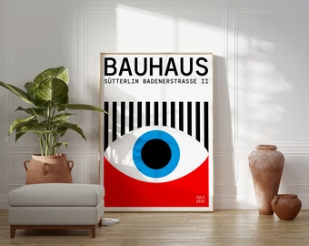 Peut inclure: Une affiche Bauhaus avec un fond à rayures noires et blanches et un grand œil avec un iris bleu et une pupille noire. L'œil est sur un fond rouge. L'affiche indique "Bauhaus" et "Sütterlin Badenerstrasse II" en texte noir. L'affiche comprend également la date "Juli 1923" en texte noir.