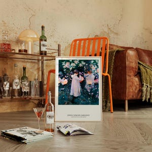 May include: A framed art print featuring John Singer Sargent's painting Carnation, Lily, Lily, Rose, depicting two figures in white dresses lighting lanterns in a garden. The print includes the artist's name and title in black text at the bottom.