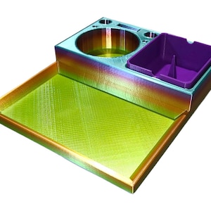 May include: A multi-colored tray with a built-in ashtray and cup holder. The tray has a rectangular base with a raised edge and a textured surface. The ashtray is purple, and the cup holder is a circular shape. The tray is made of a rainbow-colored material.