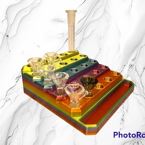 May include: A multi-colored, tiered tray with multiple glass bowls and a clear glass tube. The tray is designed with a rainbow gradient and features various holes to hold the glass bowls. The clear glass tube is positioned at the top of the tray.