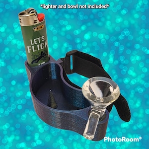 May include: A dark blue and purple 3D-printed accessory with a holder for a lighter and a glass bowl. The lighter holder has the text "LET'S FLICK" printed on it. The accessory has a black adjustable strap.