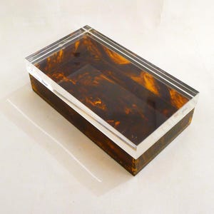 May include: A rectangular box with a clear acrylic lid and a brown, marbled base. The lid is slightly raised above the base.
