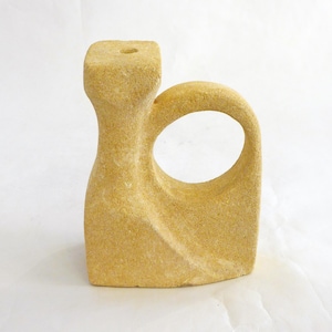 Puede incluir: Una escultura abstracta de color beige claro con una base rectangular y un elemento curvo en forma de asa. La parte superior presenta una forma cuadrada con un pequeño agujero. La escultura tiene una superficie texturizada y un diseño moderno.