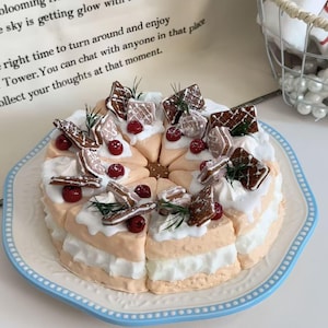 Op de afbeelding: Een decoratieve taart met meerdere lagen crème en perzikglazuur, gegarneerd met witte glazuur, peperkoekkoekjes, rode bessen en rozemarijntakjes. De taart staat op een wit bord met een blauwe rand.