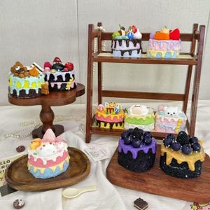 May include: A collection of miniature, colorful cakes with various toppings, including fruit, bears, and other decorative elements. Some cakes are on a wooden tiered shelf and others on wooden serving plates. The cakes have a variety of frosting colors.