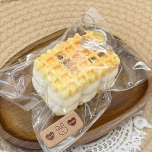 Op de afbeelding: Een wafelvormige sleutelhanger met een vorkbedel en de tekst "Get Through". De wafel heeft een goudbruine bovenkant met donkere chocoladeschilfers en een witte basis. Het is verpakt in doorzichtig plastic.