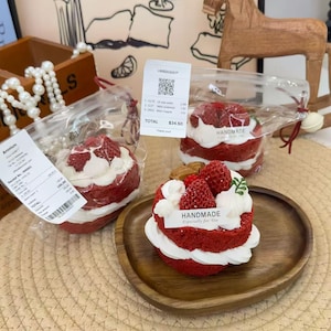 Op de afbeelding: Rode fluwelen cakes met witte glazuur en verse aardbeien. Eén cake ligt op een houten bord, en twee zitten in doorzichtige plastic zakken. De cakes zijn voorzien van het label "HANDMADE Especially for You."