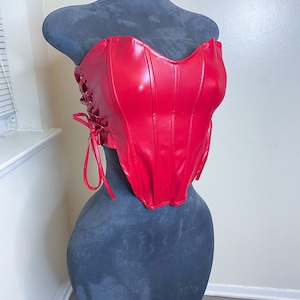 May include: A red faux leather corset with a sweetheart neckline and lace-up detail at the back.