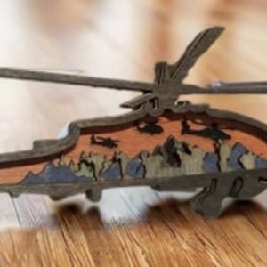 Może przedstawiać: Drewniany wycinany model helikoptera z kamuflażem. Helikopter jest pomalowany w odcieniach brązu, zieleni i błękitu. Model jest szczegółowym przedstawieniem wojskowego helikoptera.