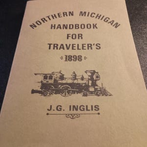 May include: A tan-colored handbook titled "Northern Michigan Handbook for Traveler's 1898" with a black illustration of a train. The author's name, J.G. Inglis, is printed below the train illustration.