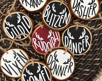 May include: Ten round wooden decorations with white paint and black lettering. Each decoration features a reindeer name from the song "Rudolph the Red-Nosed Reindeer" including:  "Comet", "Dancer", "Dasher", "Donner", "Blitzen", "Vixen", "Prancer", "Cupid", "Rudolph", and "Comet".