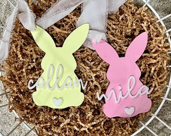 May include: Two pastel colored bunny shaped ornaments with white lettering. The yellow bunny says "callan" and the pink bunny says "mila".