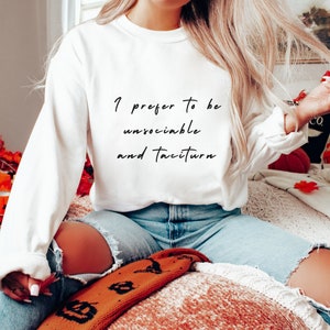 Puede incluir: Sudadera blanca de manga larga con el texto "I prefer to be unsociable and taciturn" impreso en negro.