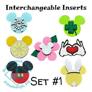 May include: A collection of interchangeable inserts in the shape of Mickey Mouse ears. Designs include a snowflake, a lemon slice, a four-leaf clover, a flower, a heart, and a Minnie Mouse design. The text "Interchangeable Inserts" and "Set #1" are also visible.